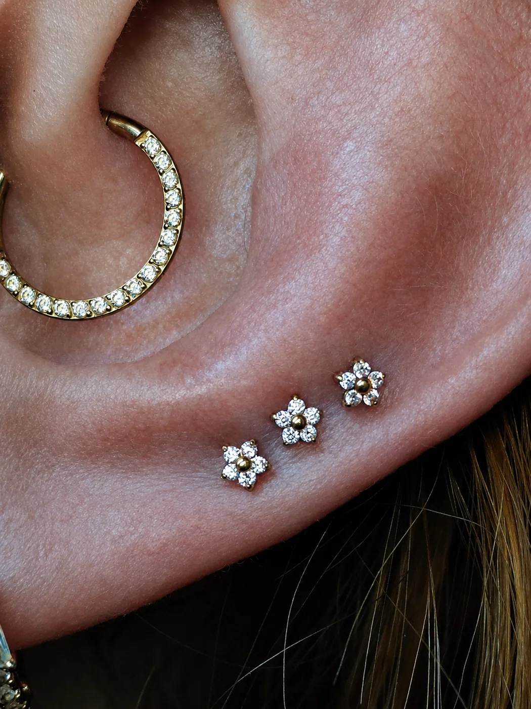 Piercing daith com argola cravejada e lóbulo com joias de flor